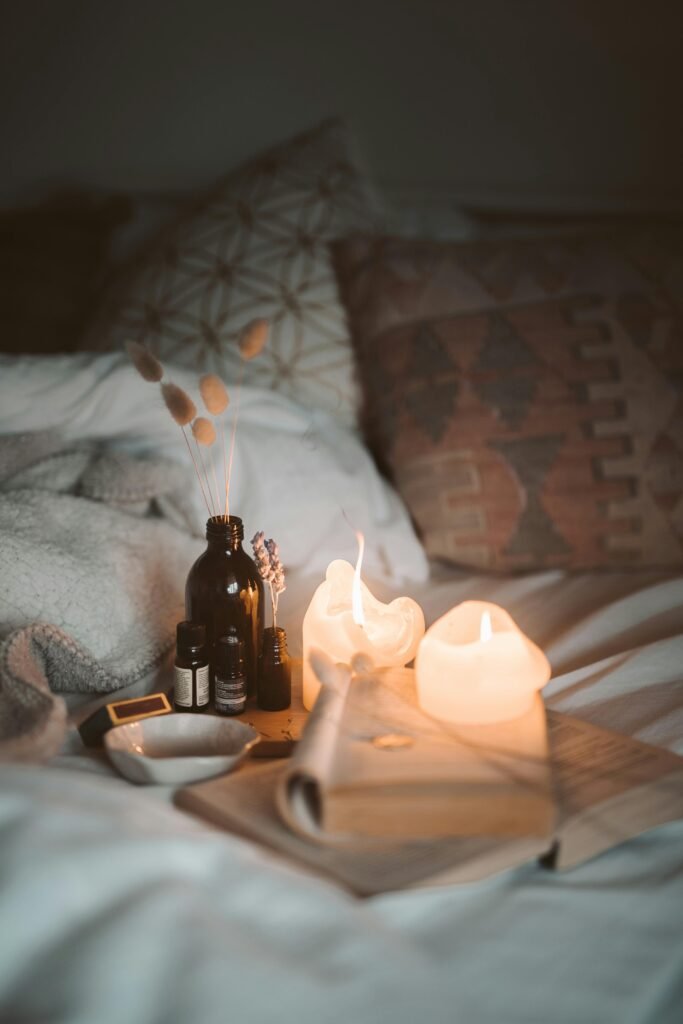 A warm and cozy bedroom scene with burning candles, a book, and essential oils creating a relaxing atmosphere.